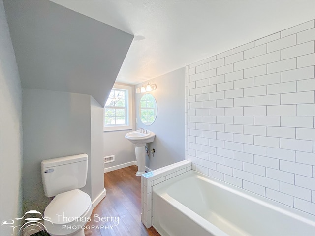 full bath featuring toilet, wood finished floors, visible vents, baseboards, and a tub