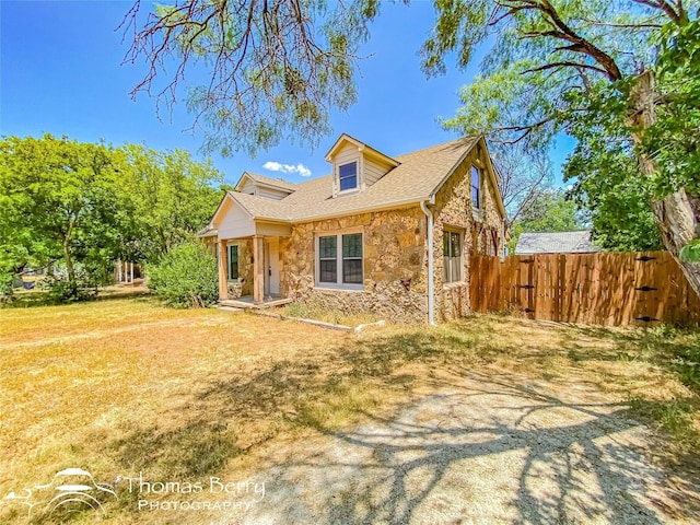 view of front facade featuring stone siding, roof with shingles, fence, and a front yard