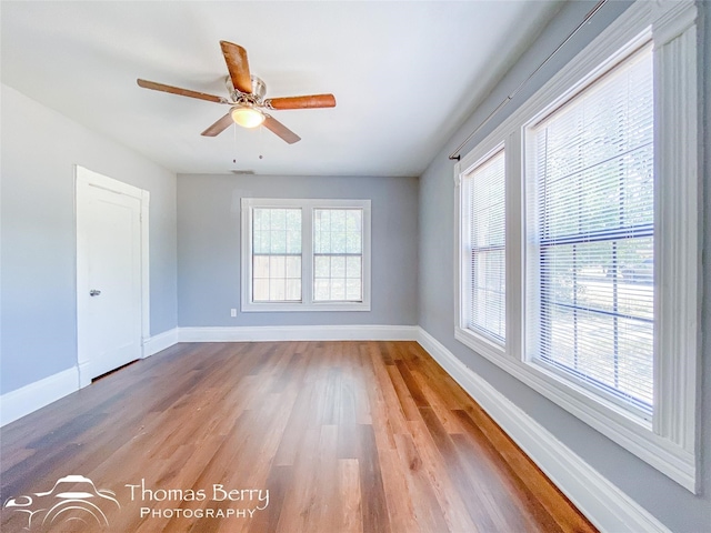 unfurnished room featuring a healthy amount of sunlight, wood finished floors, a ceiling fan, and baseboards