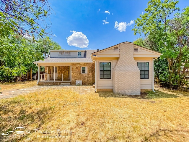 back of property featuring stone siding, a porch, and a yard