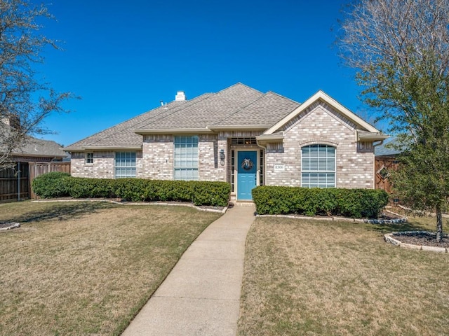 view of front facade featuring brick siding, a shingled roof, fence, and a front yard