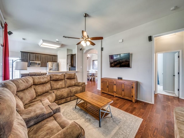 living area with arched walkways, dark wood-style flooring, ceiling fan, and baseboards