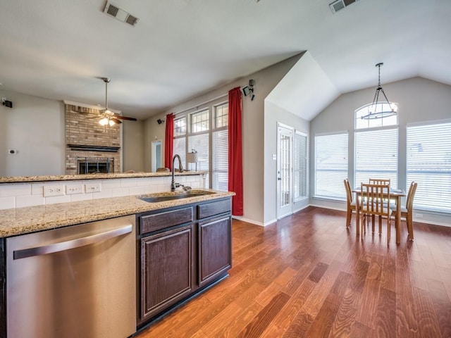 kitchen with a sink, visible vents, a brick fireplace, dishwasher, and light wood finished floors