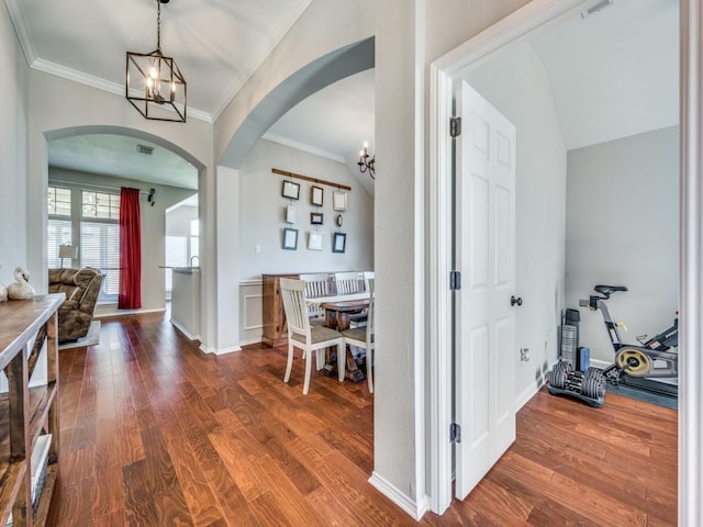 interior space featuring ornamental molding, arched walkways, wood finished floors, and an inviting chandelier