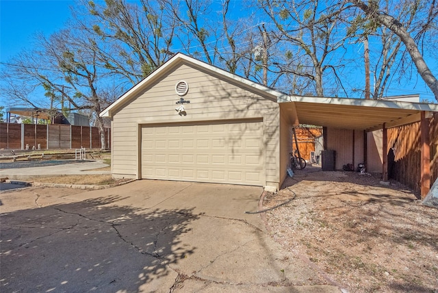 garage with driveway, fence, and a carport