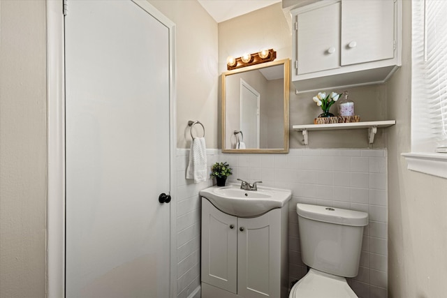 half bathroom with a wainscoted wall, vanity, toilet, and tile walls