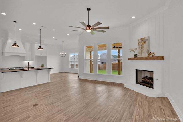 unfurnished living room with crown molding, light wood-style floors, a fireplace with raised hearth, and ceiling fan with notable chandelier