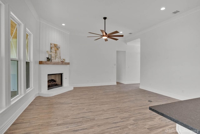 unfurnished living room with a fireplace, light wood-style flooring, a ceiling fan, visible vents, and ornamental molding