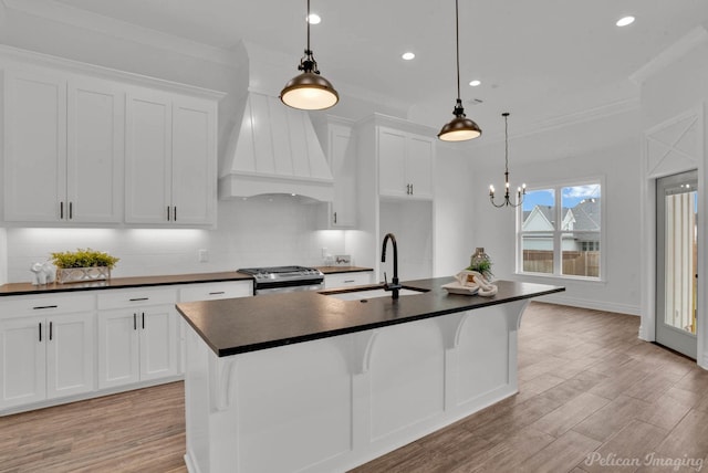 kitchen featuring dark countertops, a sink, stainless steel range with gas cooktop, custom range hood, and recessed lighting