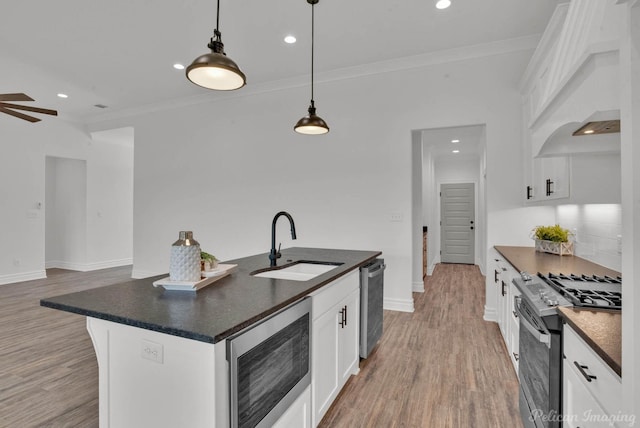 kitchen featuring crown molding, appliances with stainless steel finishes, dark countertops, a sink, and premium range hood