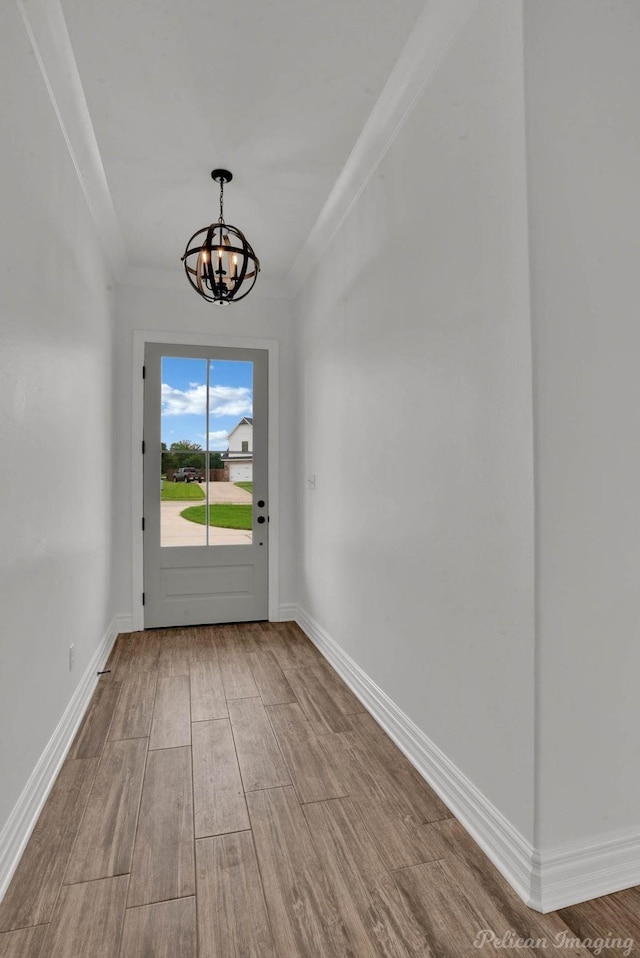 entryway with an inviting chandelier, baseboards, crown molding, and wood finished floors
