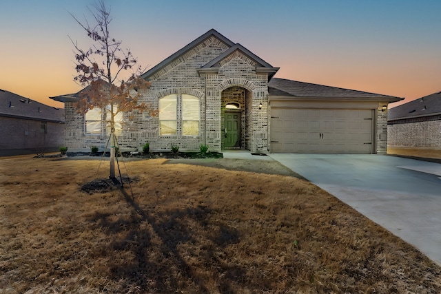 french country home featuring a garage, concrete driveway, and brick siding