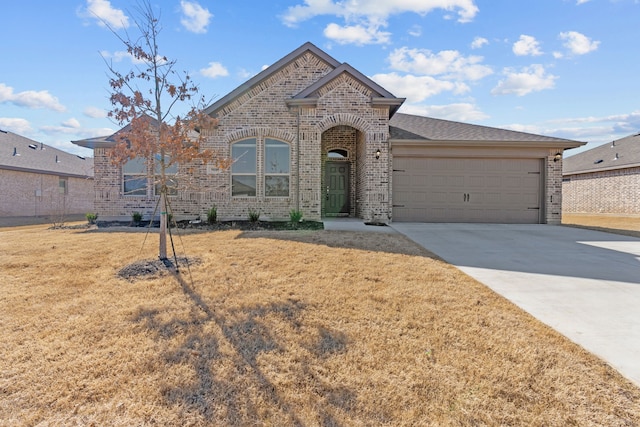 french country inspired facade with driveway, an attached garage, a front lawn, and brick siding