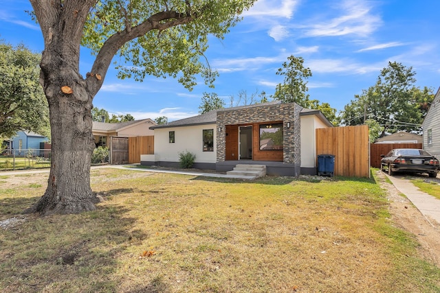 view of front facade with stone siding, a front yard, fence, and stucco siding