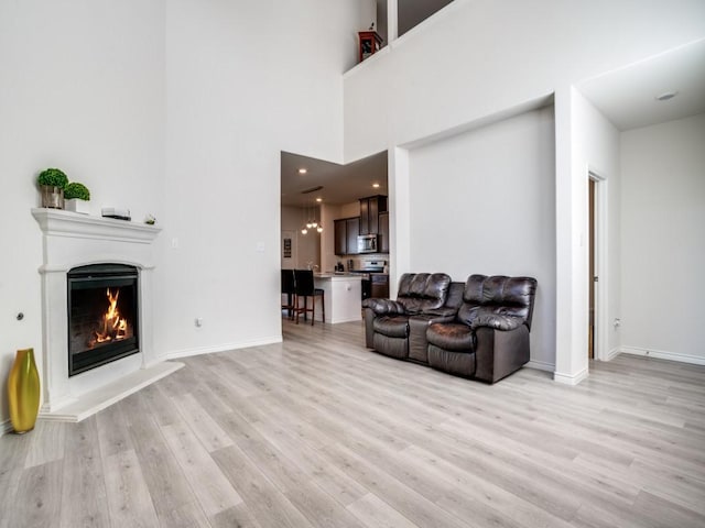 living area featuring light wood finished floors, a warm lit fireplace, and baseboards