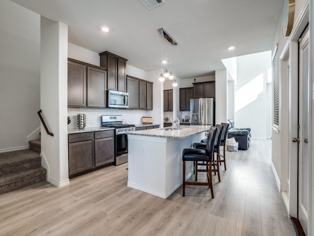 kitchen with dark brown cabinetry, appliances with stainless steel finishes, light wood-style floors, and backsplash