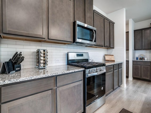 kitchen featuring light stone countertops, stainless steel appliances, dark brown cabinets, light wood-type flooring, and decorative backsplash