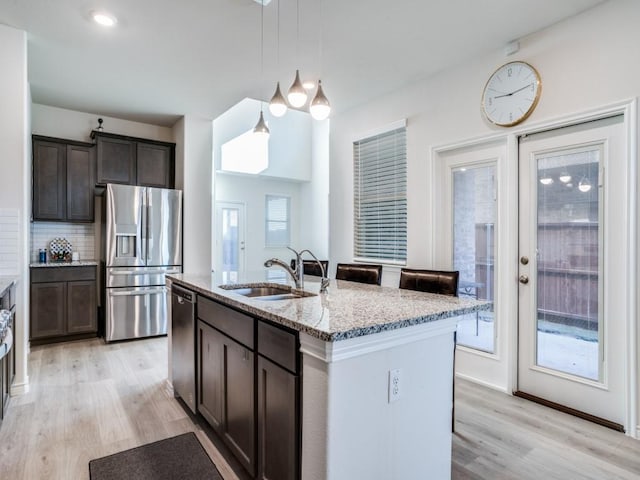 kitchen with tasteful backsplash, appliances with stainless steel finishes, light stone countertops, dark brown cabinets, and a sink