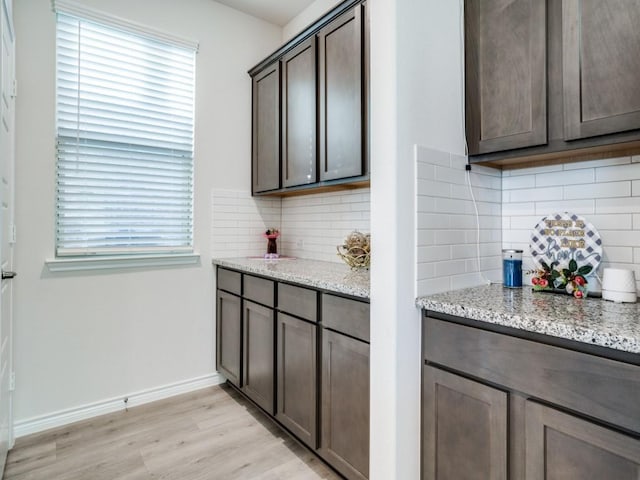 kitchen featuring baseboards, dark brown cabinets, light stone counters, and light wood-style floors