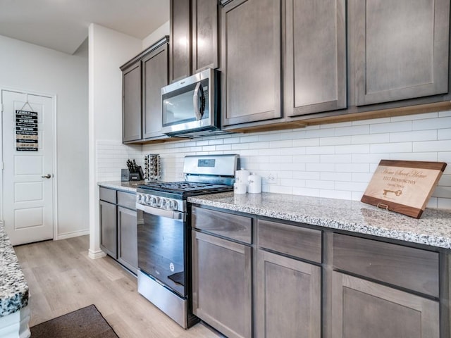 kitchen with light stone counters, light wood finished floors, stainless steel appliances, backsplash, and dark brown cabinets