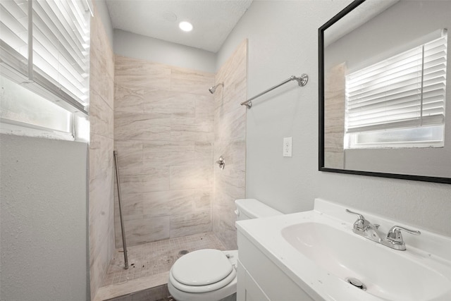 bathroom with toilet, a textured wall, a tile shower, and vanity