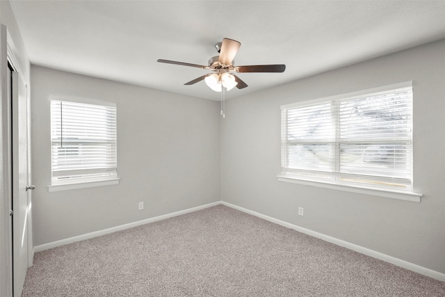 carpeted spare room featuring a wealth of natural light, ceiling fan, and baseboards