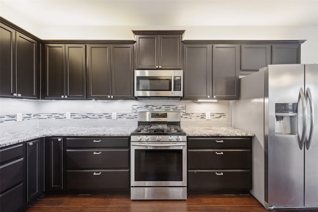 kitchen featuring appliances with stainless steel finishes, dark wood-style flooring, decorative backsplash, and light stone countertops