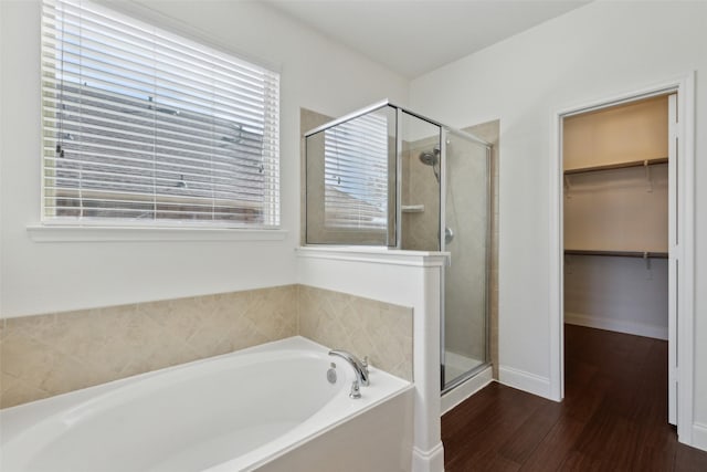 bathroom featuring baseboards, wood finished floors, a walk in closet, a shower stall, and a bath