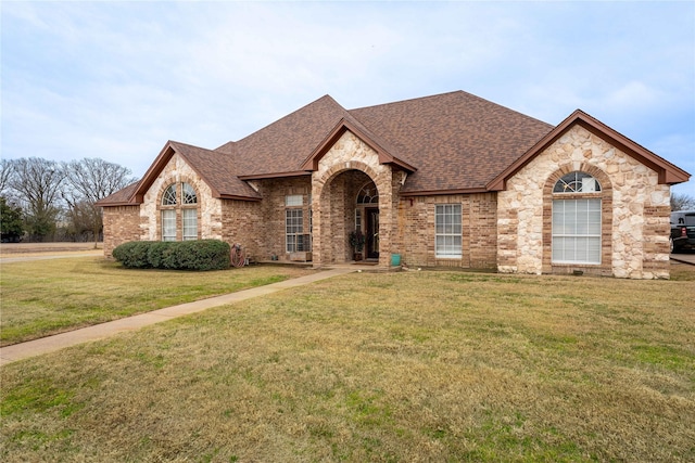 french country home featuring a front lawn, roof with shingles, and brick siding