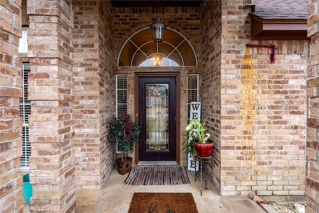 view of exterior entry with roof with shingles and brick siding