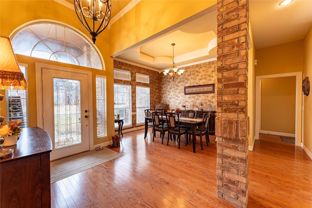 interior space with crown molding, a raised ceiling, an inviting chandelier, wood finished floors, and baseboards