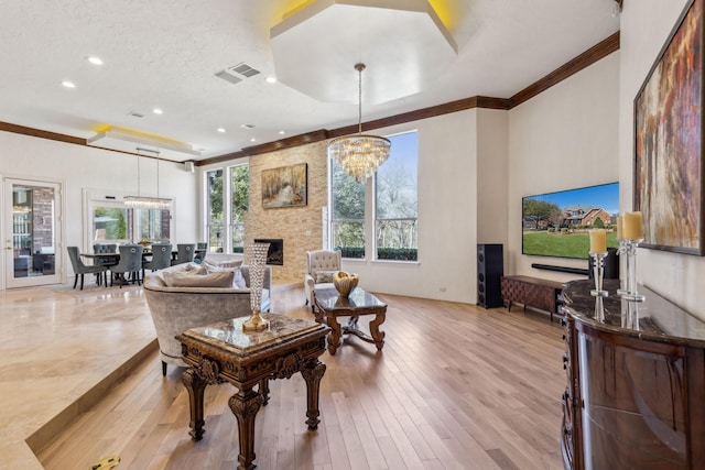 living room featuring visible vents, an inviting chandelier, light wood-style flooring, ornamental molding, and a large fireplace