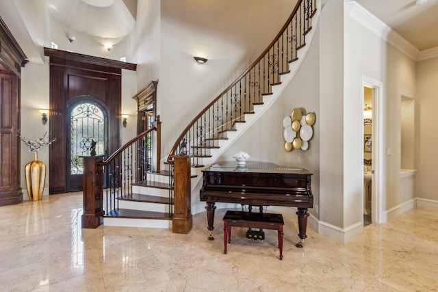 foyer entrance with marble finish floor, ornamental molding, baseboards, and a towering ceiling