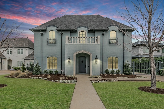 french country inspired facade with a yard, brick siding, fence, and a balcony