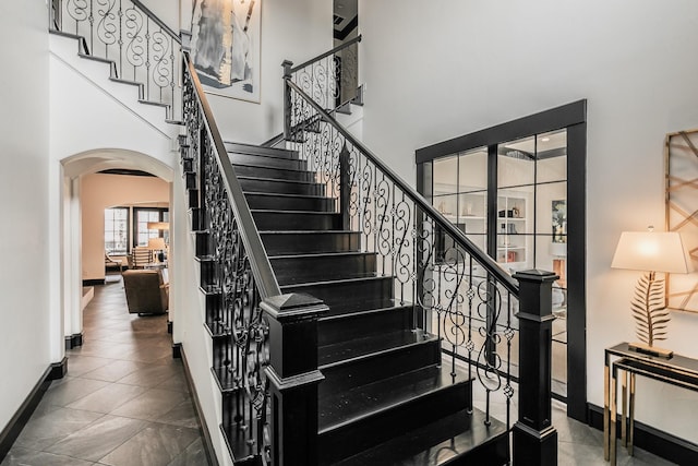 stairs featuring arched walkways, a towering ceiling, and baseboards