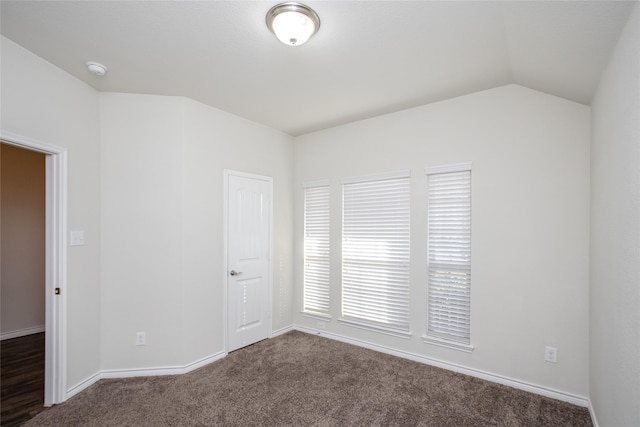 spare room featuring dark colored carpet, vaulted ceiling, and baseboards