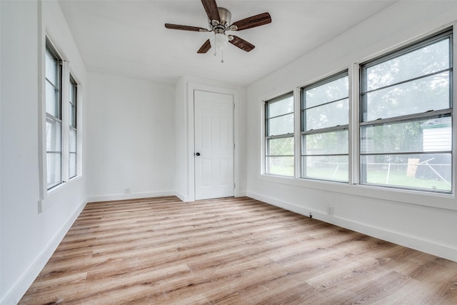 spare room with light wood-type flooring, a ceiling fan, and baseboards