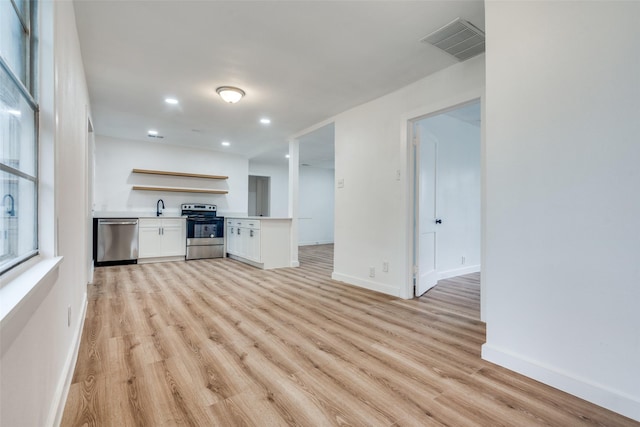 unfurnished living room with light wood-type flooring, a sink, visible vents, and baseboards