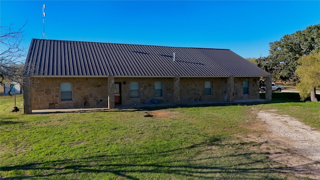 back of property featuring stone siding, a lawn, and metal roof