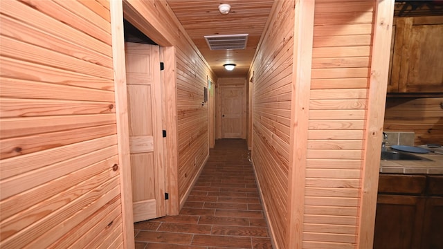 hall with visible vents, dark wood-type flooring, a sink, wooden walls, and wooden ceiling