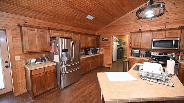 kitchen with tile countertops, wooden walls, stainless steel appliances, wood ceiling, and vaulted ceiling