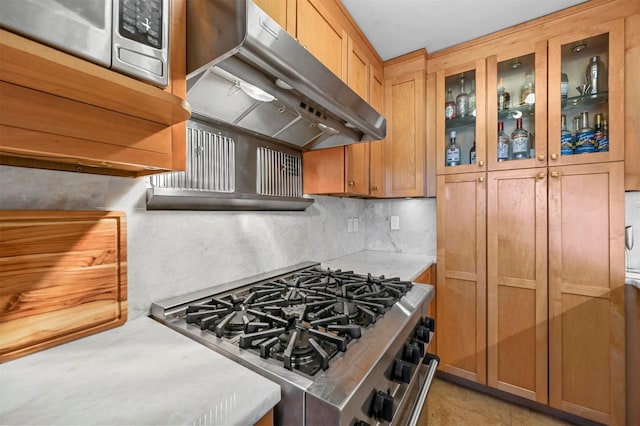 kitchen with under cabinet range hood, light countertops, stainless steel range with gas cooktop, decorative backsplash, and glass insert cabinets