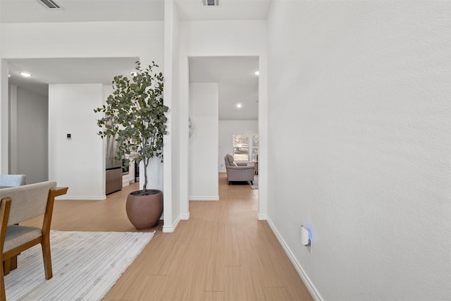 hall with visible vents, baseboards, and light wood-style floors