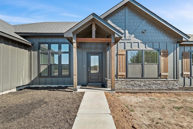 view of exterior entry featuring board and batten siding and a shingled roof