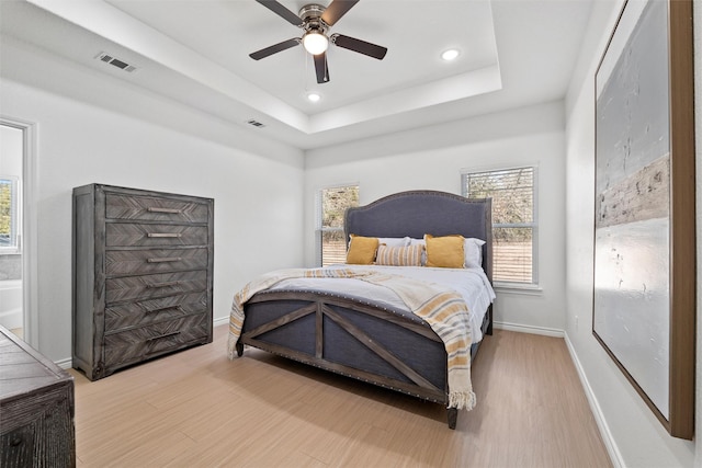 bedroom featuring visible vents, a raised ceiling, baseboards, and wood finished floors