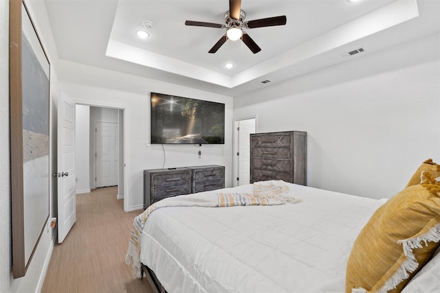 bedroom featuring visible vents, baseboards, light wood-style flooring, recessed lighting, and a raised ceiling