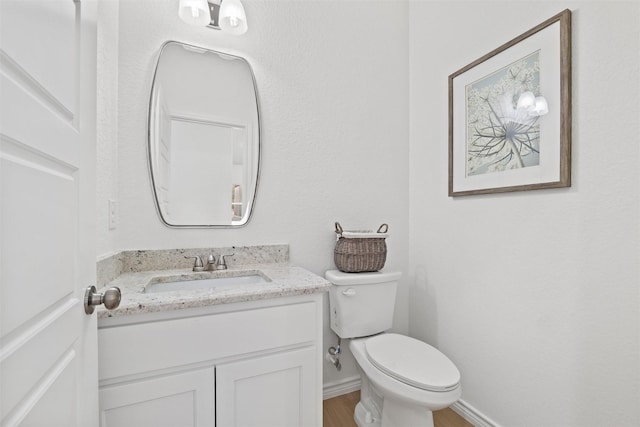 bathroom with vanity, toilet, wood finished floors, and baseboards