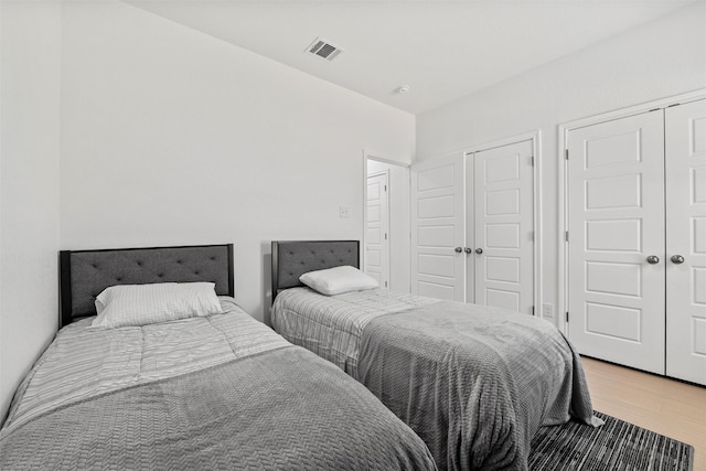 bedroom featuring visible vents, light wood-type flooring, and multiple closets