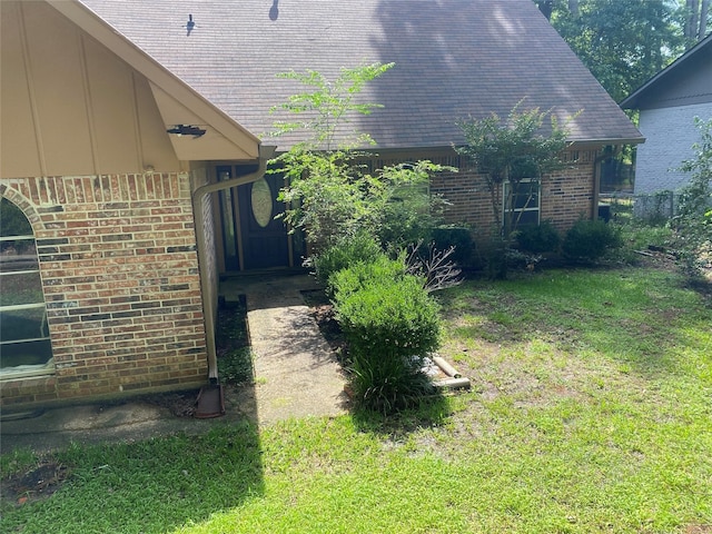 view of home's exterior with a yard, brick siding, and roof with shingles