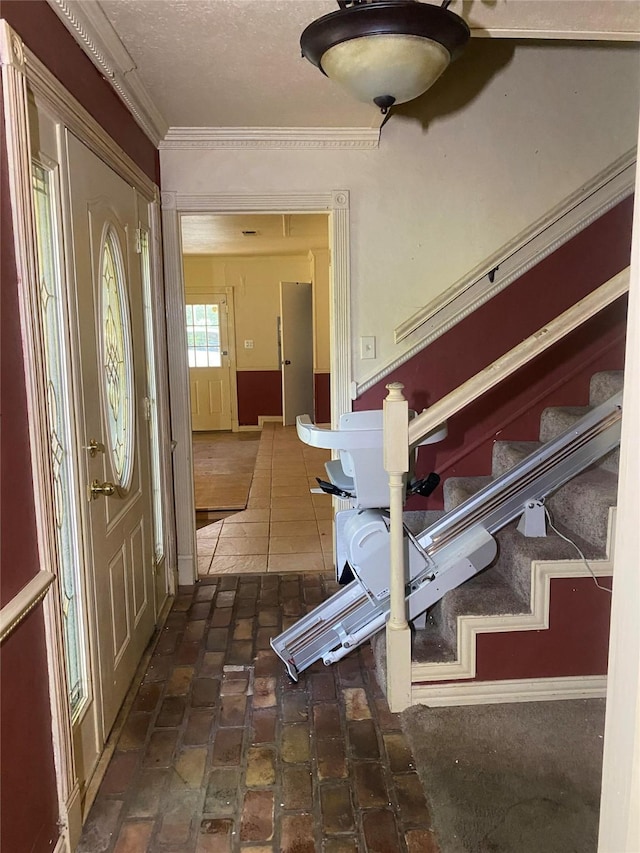 entryway with stairs, a textured ceiling, and brick floor